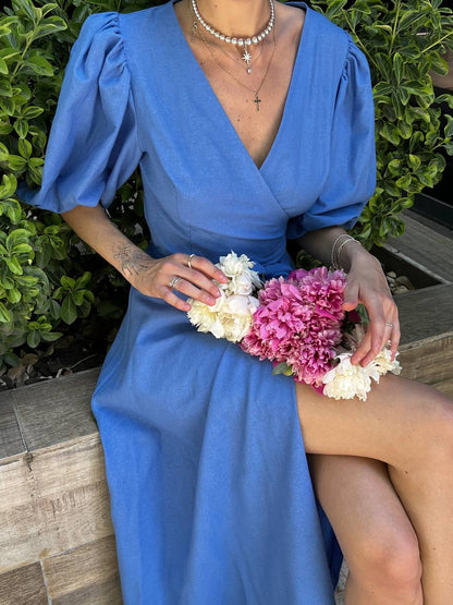 Person wearing a blue dress holding flowers against a green bush background