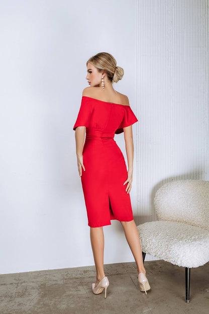 Woman wearing a red off-shoulder dress standing against a white wall.