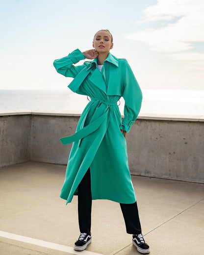Person wearing a teal trench coat on a rooftop with a clear sky.