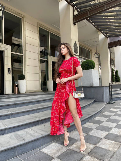 Woman in a red dress standing on a sidewalk in front of a building.