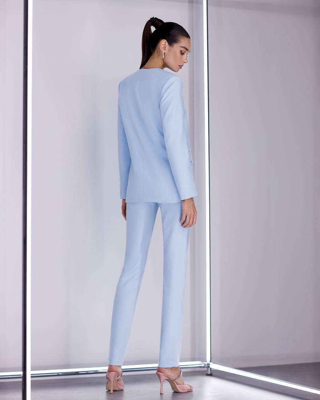 Woman wearing a light blue suit standing in a minimalistic room with white walls and a gray floor.
