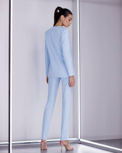 Woman wearing a light blue suit standing in a minimalistic room with white walls and a gray floor.