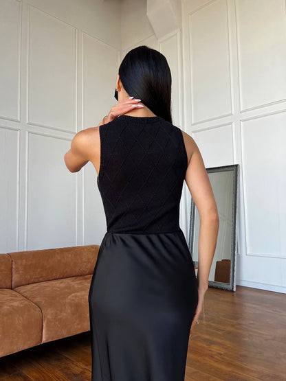 Woman wearing a black sleeveless dress standing in a room with white paneled walls and a brown sofa.