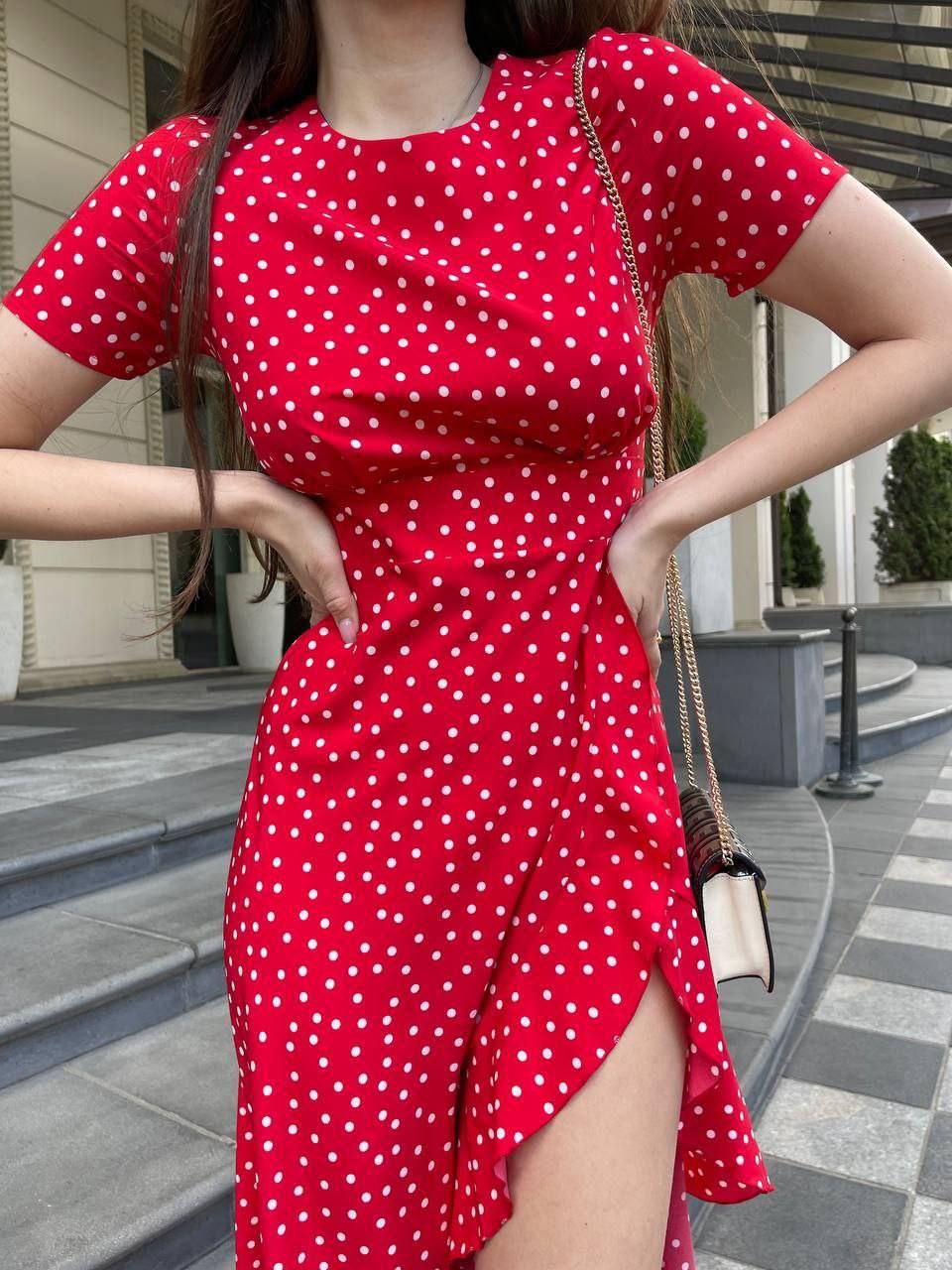 Person wearing a red polka dot dress with a gold handbag outdoors.