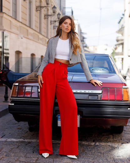 Woman in red pants and checkered jacket standing in front of a vintage car.