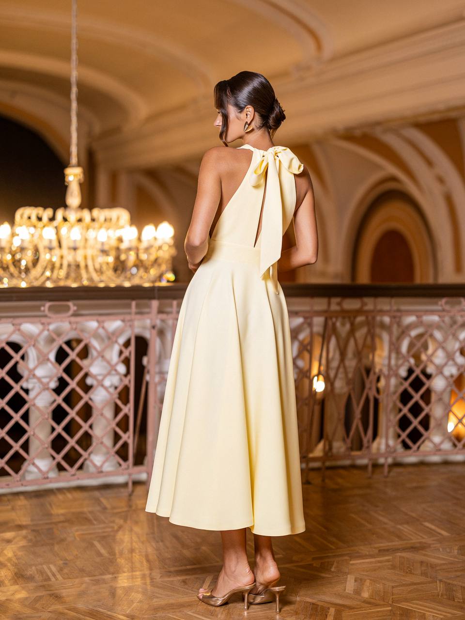 Woman in a yellow dress standing in an elegant indoor setting with chandelier.