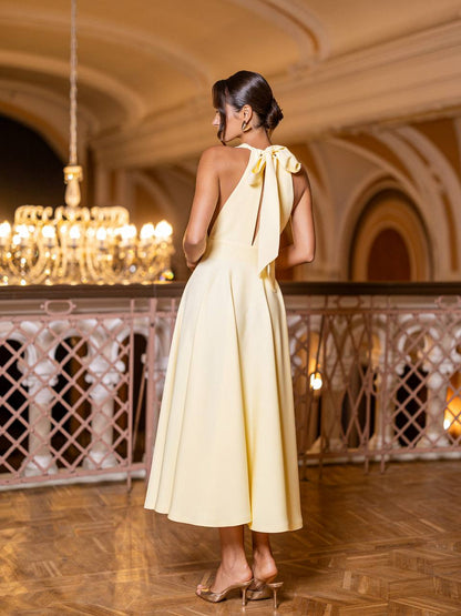 Woman in a yellow dress standing in an elegant indoor setting with chandelier.