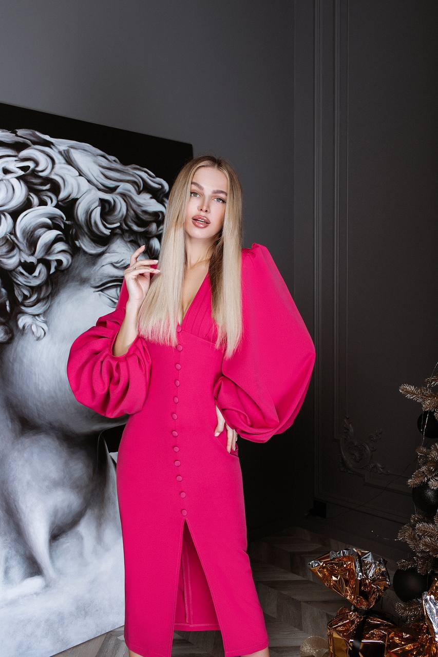 Woman in a bright pink outfit standing in a room with decorative elements.