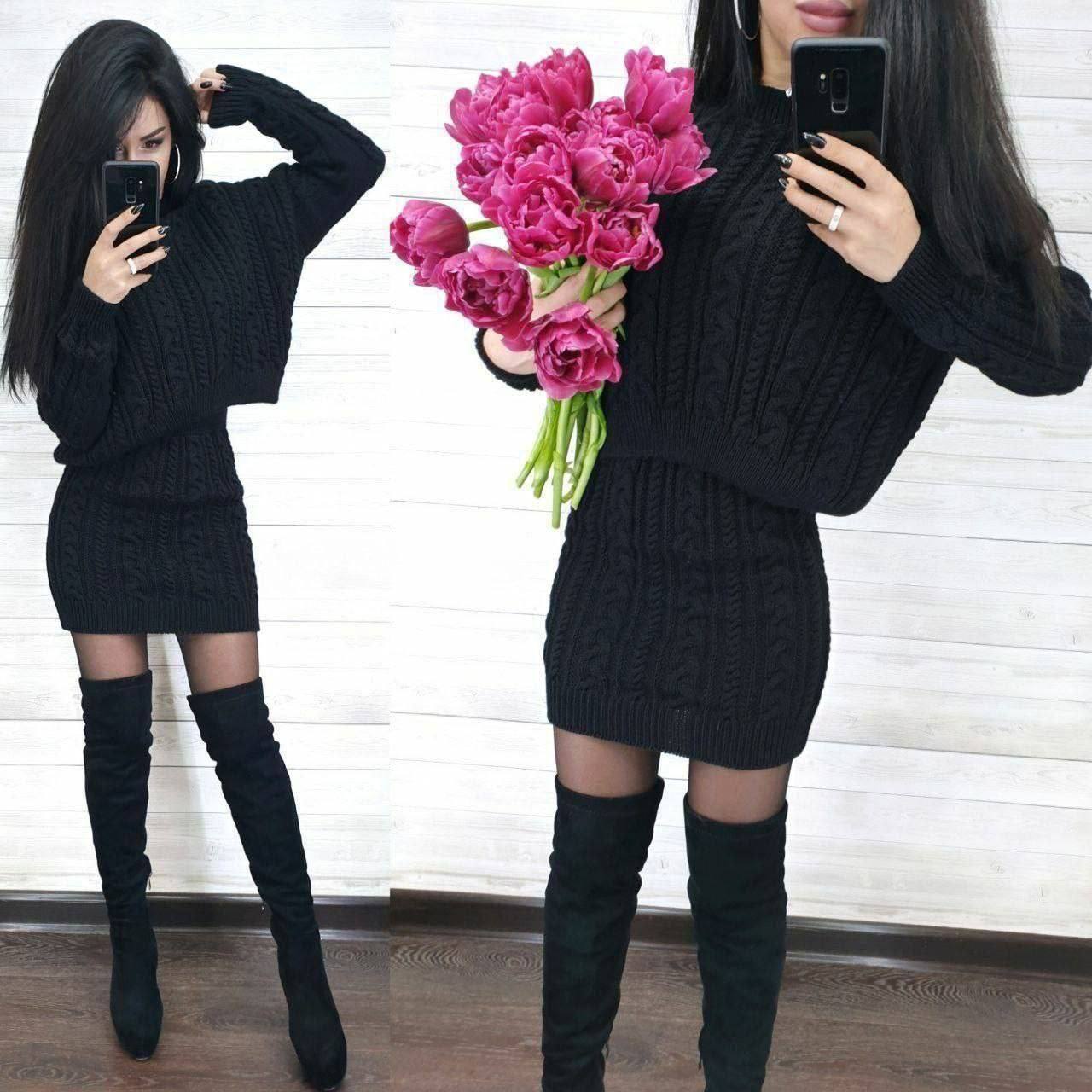 Woman in black cable knit dress and knee-high boots holding pink tulips.