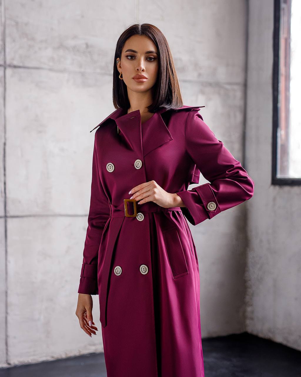 Woman wearing a purple trench coat with gold buttons against a neutral background