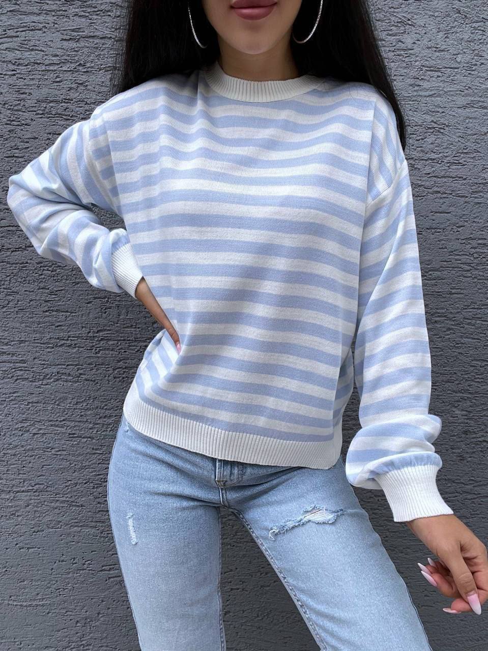 Person wearing a blue and white striped sweater and light blue jeans against a gray wall.