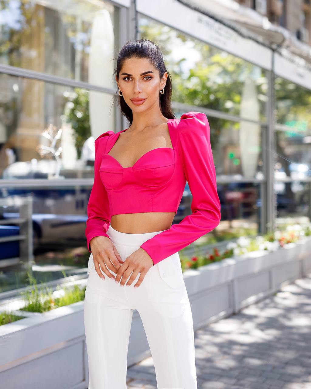 Woman wearing a bright pink top and white pants standing outdoors.