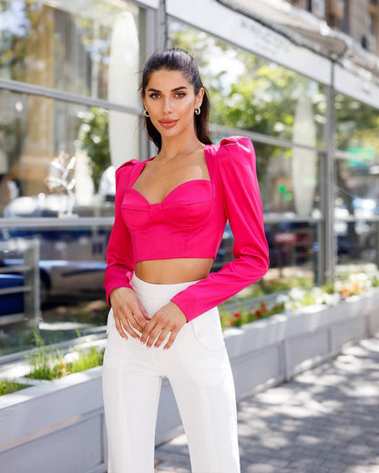 Woman wearing a bright pink top and white pants standing outdoors.