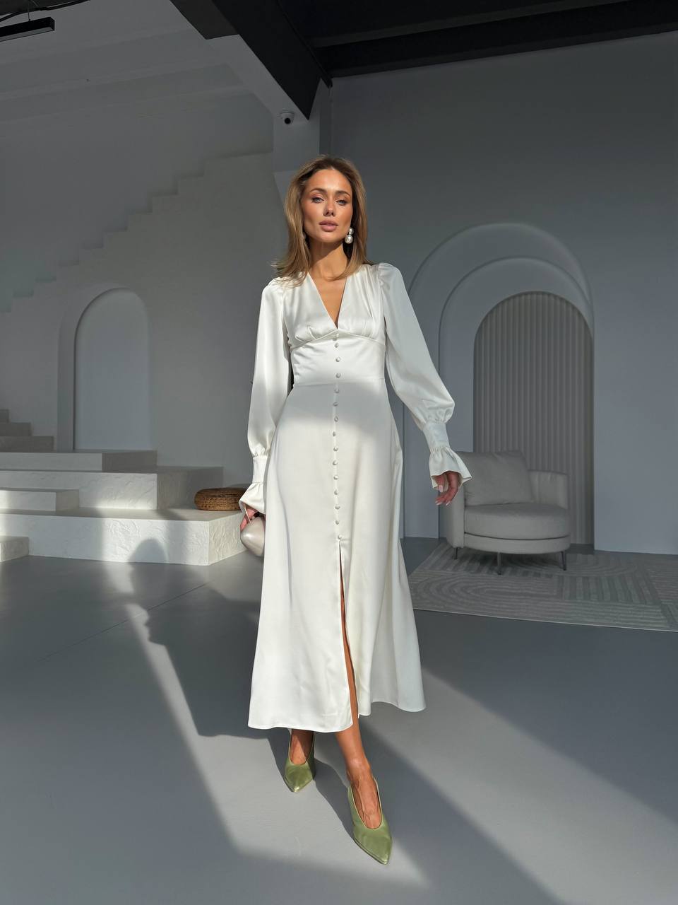 Woman in a white outfit standing in a minimalistic room with white walls and furniture.