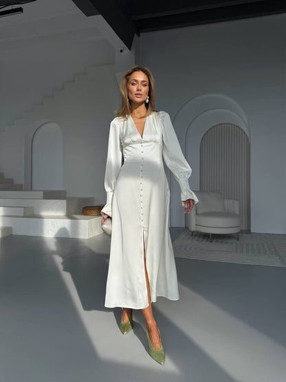 Woman in a white outfit standing in a minimalistic room with white walls and furniture.