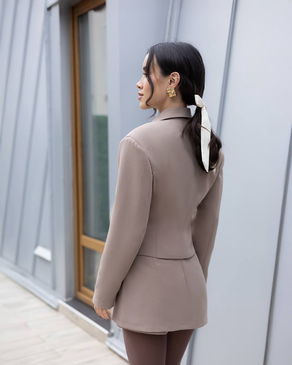 Woman in a beige suit standing against a modern building.