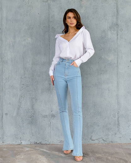 Woman wearing a white blouse and light blue jeans against a gray concrete wall.