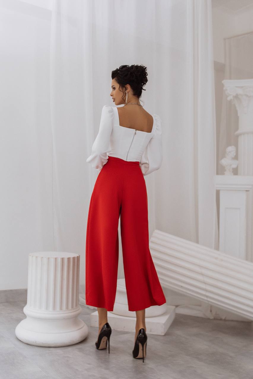 Woman in a white top and red pants standing in a room with white walls and decorative elements.