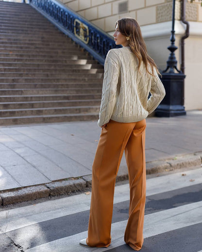 Woman in a beige sweater and brown pants walking on a city street.