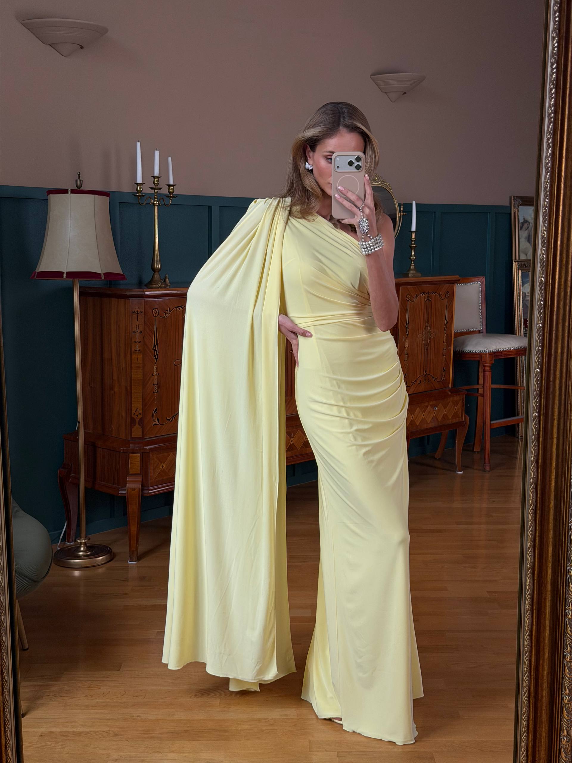 Woman in a yellow dress taking a mirror selfie in an indoor setting.