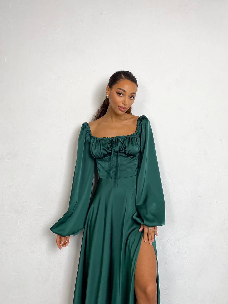 Woman wearing a green dress with long sleeves and a slit on a white background