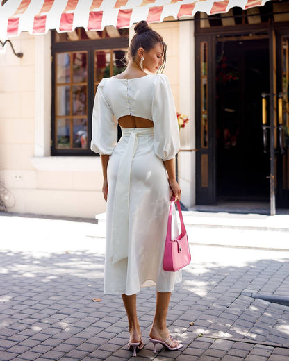 Woman in a white outfit with a pink bag walking on a street.