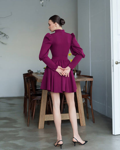 Woman in a purple dress standing in a room with wooden furniture.
