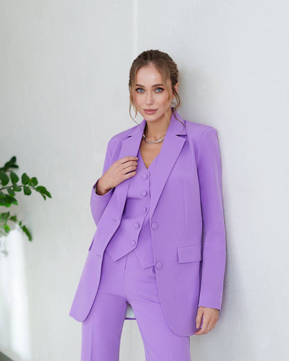 Woman wearing a purple suit standing against a white wall with a plant in the background