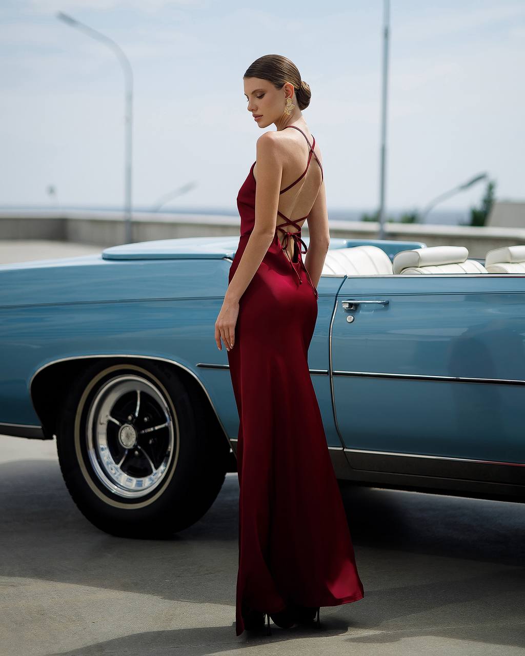 Woman in a red dress standing next to a blue vintage car on a road.