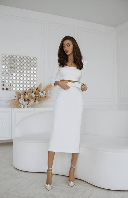 Woman in a white outfit standing in a minimalistic room with a decorative wall.