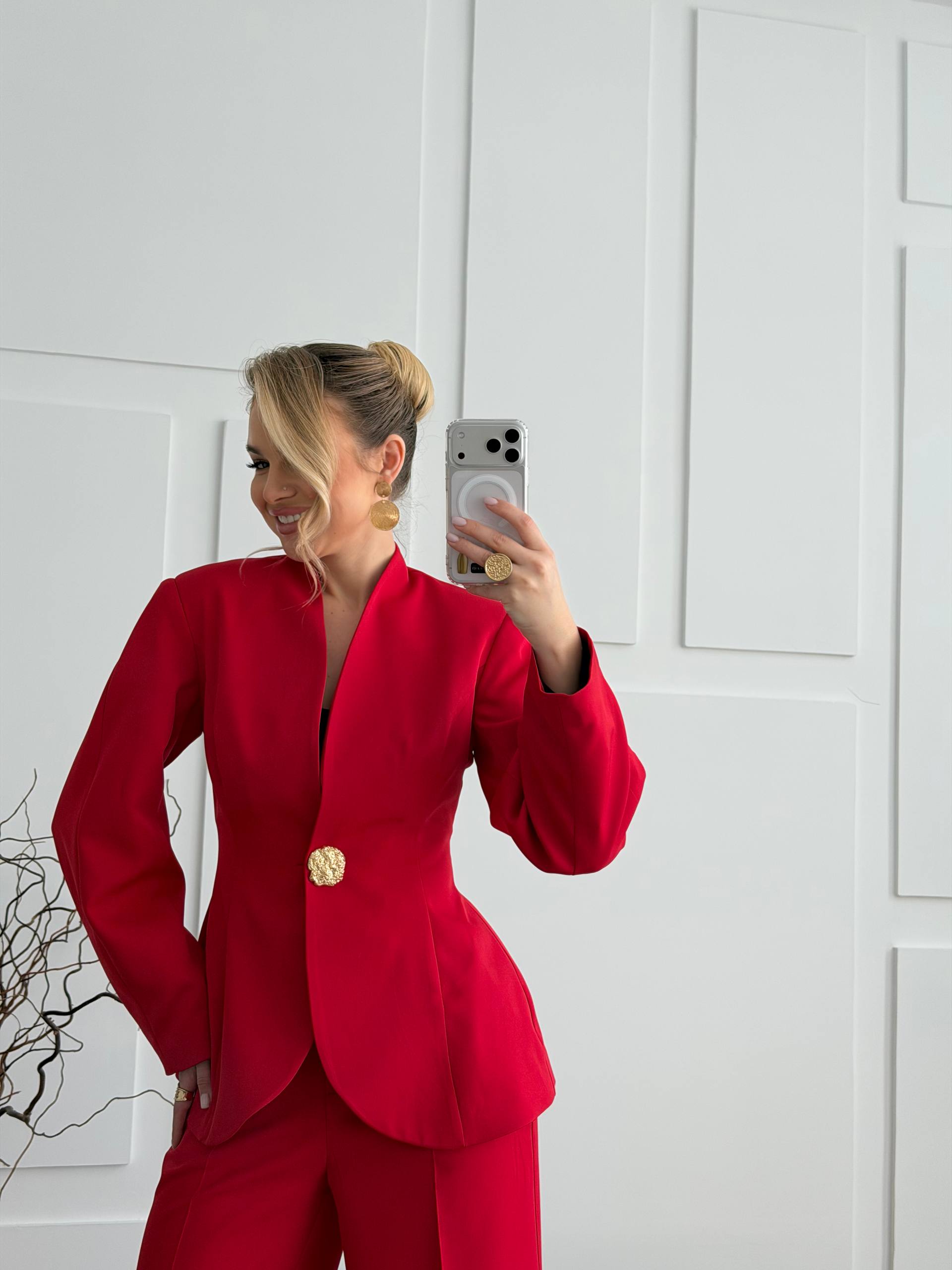 Person wearing a red suit taking a mirror selfie against a white paneled wall.