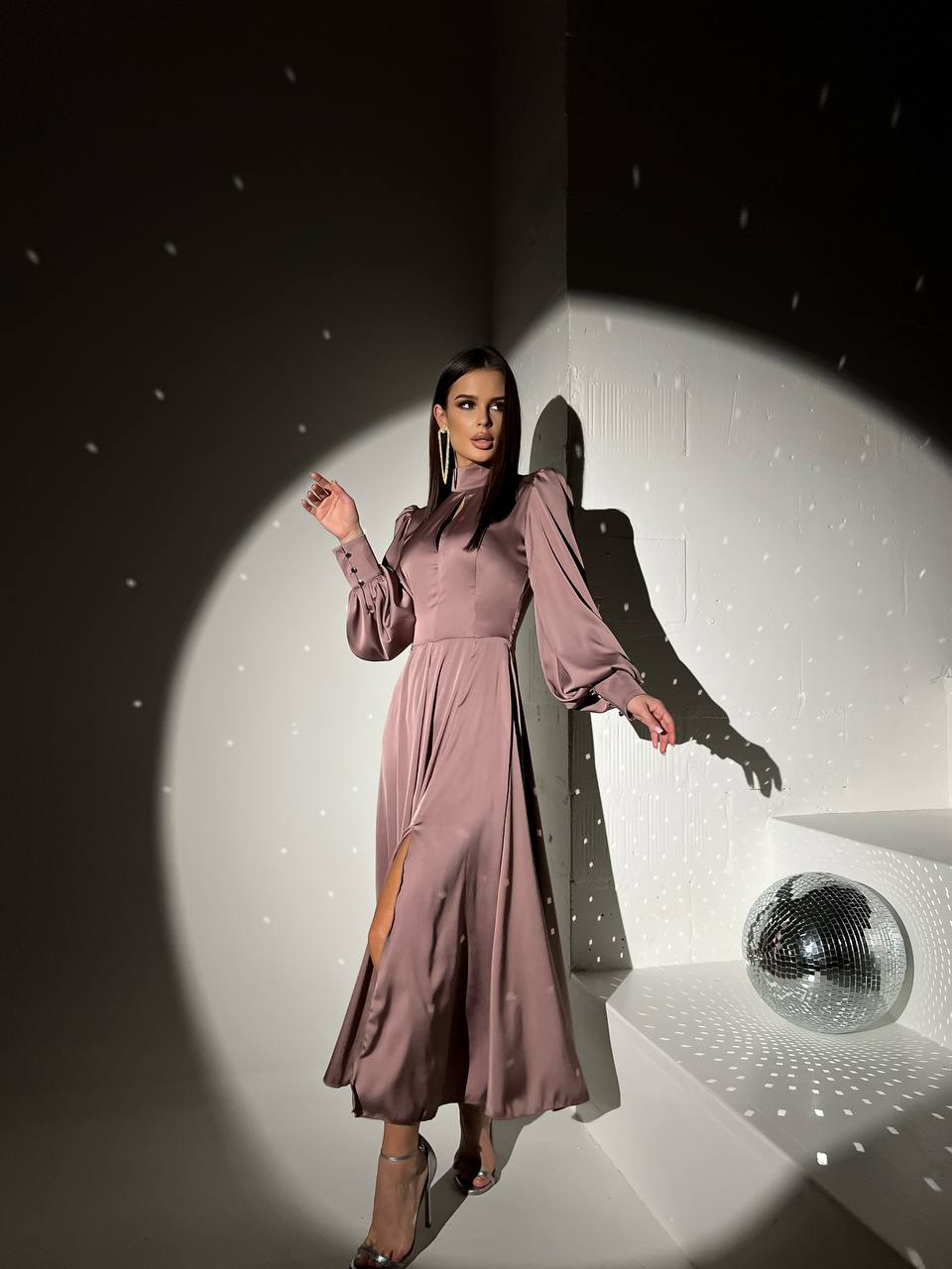 Woman in a long, light purple dress standing in a spotlight with a disco ball in the background.