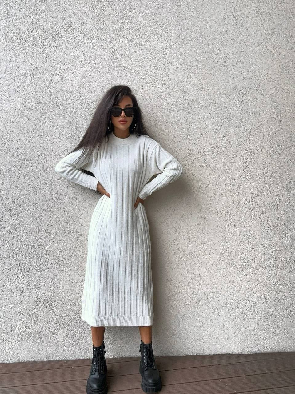 Woman wearing a white ribbed dress against a plain wall