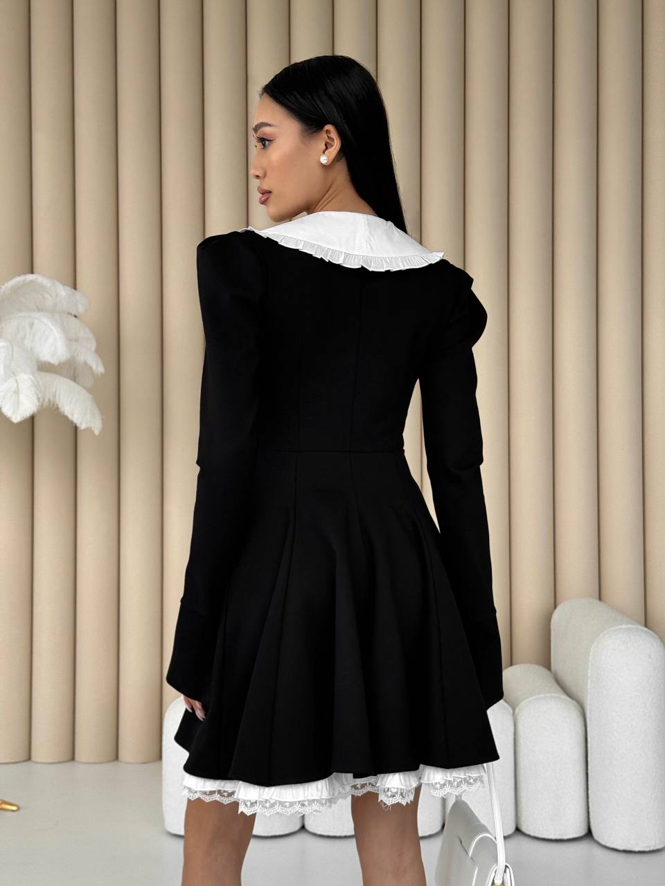 Woman wearing a black dress with white lace details in a minimalistic setting.