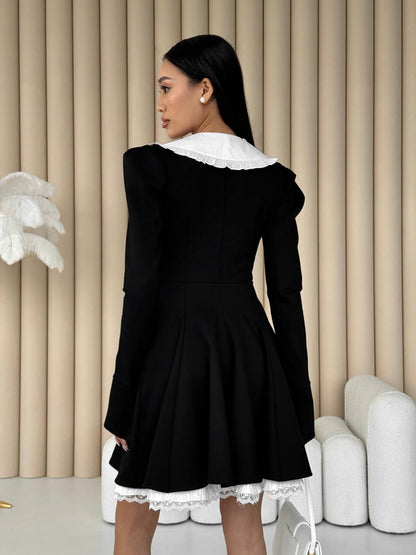 Woman wearing a black dress with white lace details in a minimalistic setting.