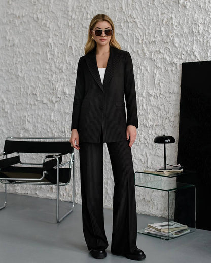 Woman in a black pinstripe suit standing in a modern interior setting.
