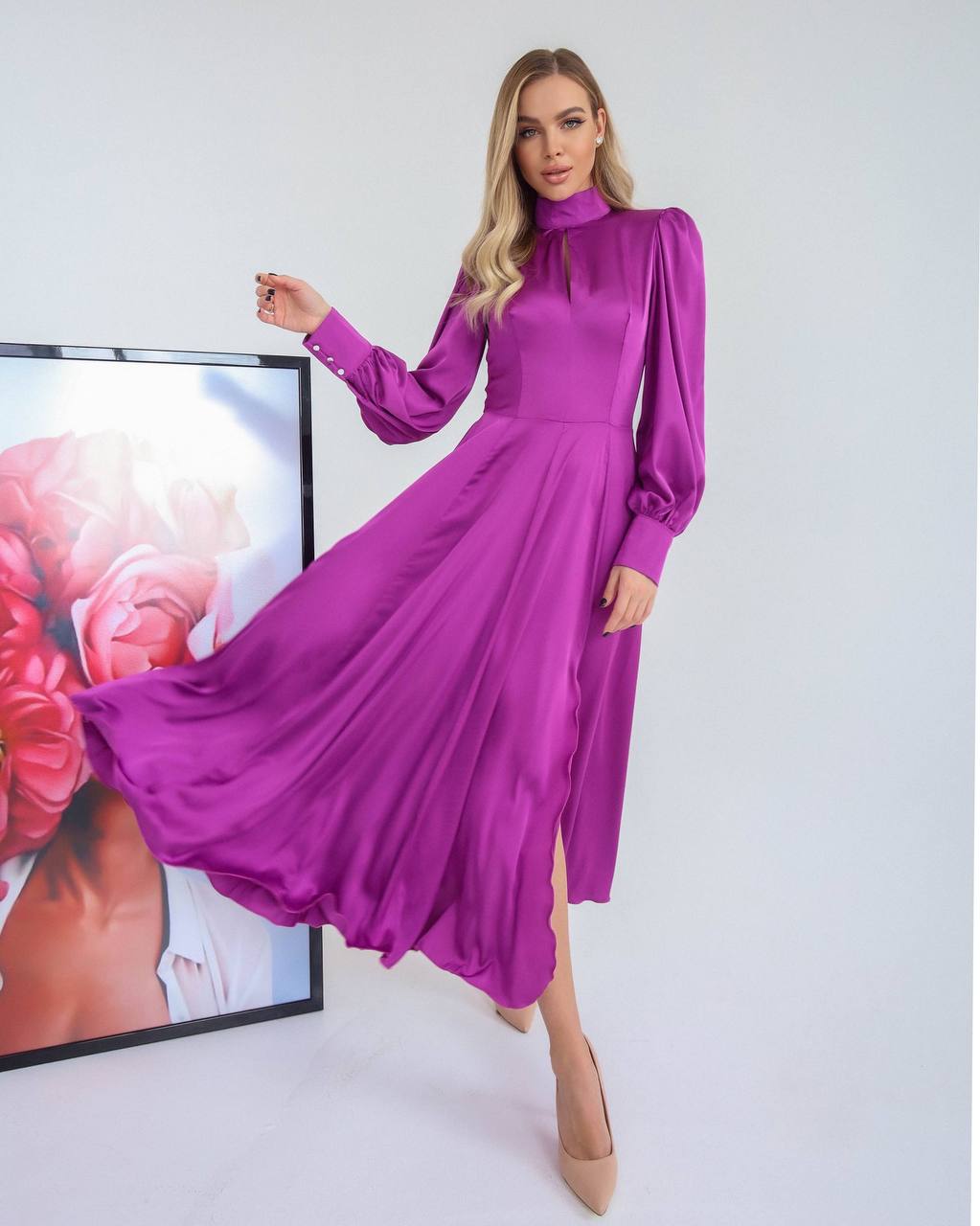 Woman wearing a purple dress with long sleeves and a high neckline, standing against a white background.