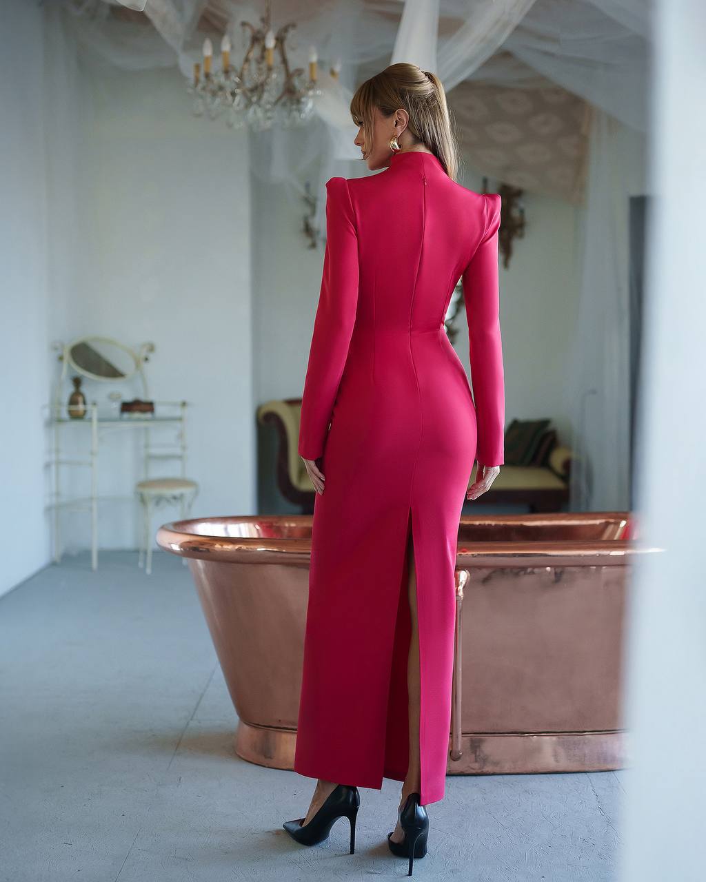 Woman in a red dress standing in a stylish room with a chandelier and bathtub.