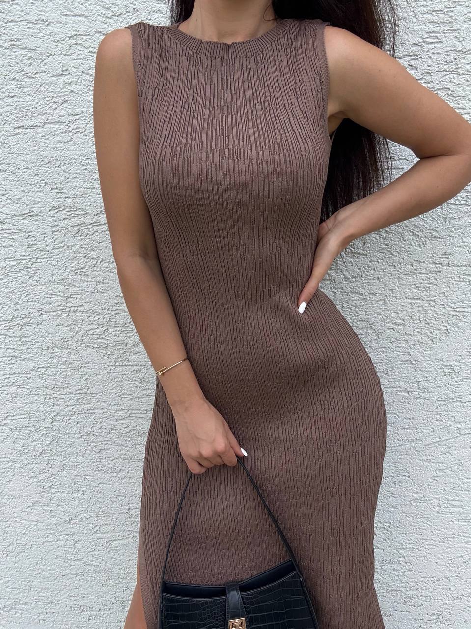 Woman wearing a brown ribbed dress against a light gray wall