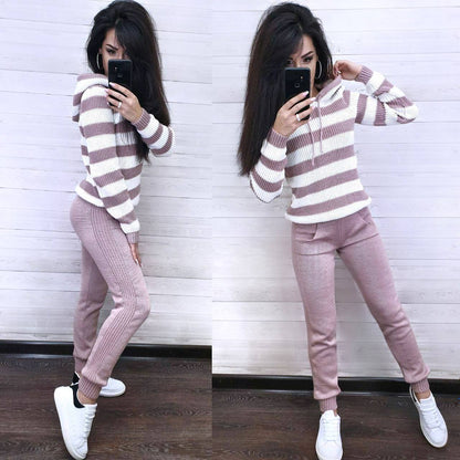 Woman wearing a striped sweater and pink pants against a white wall.