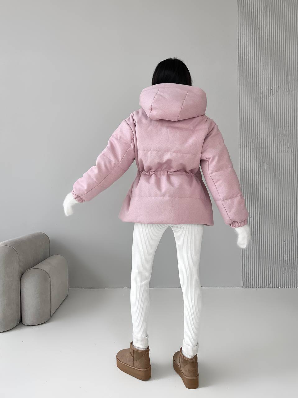 Person wearing a pink puffer jacket in a minimalistic room.