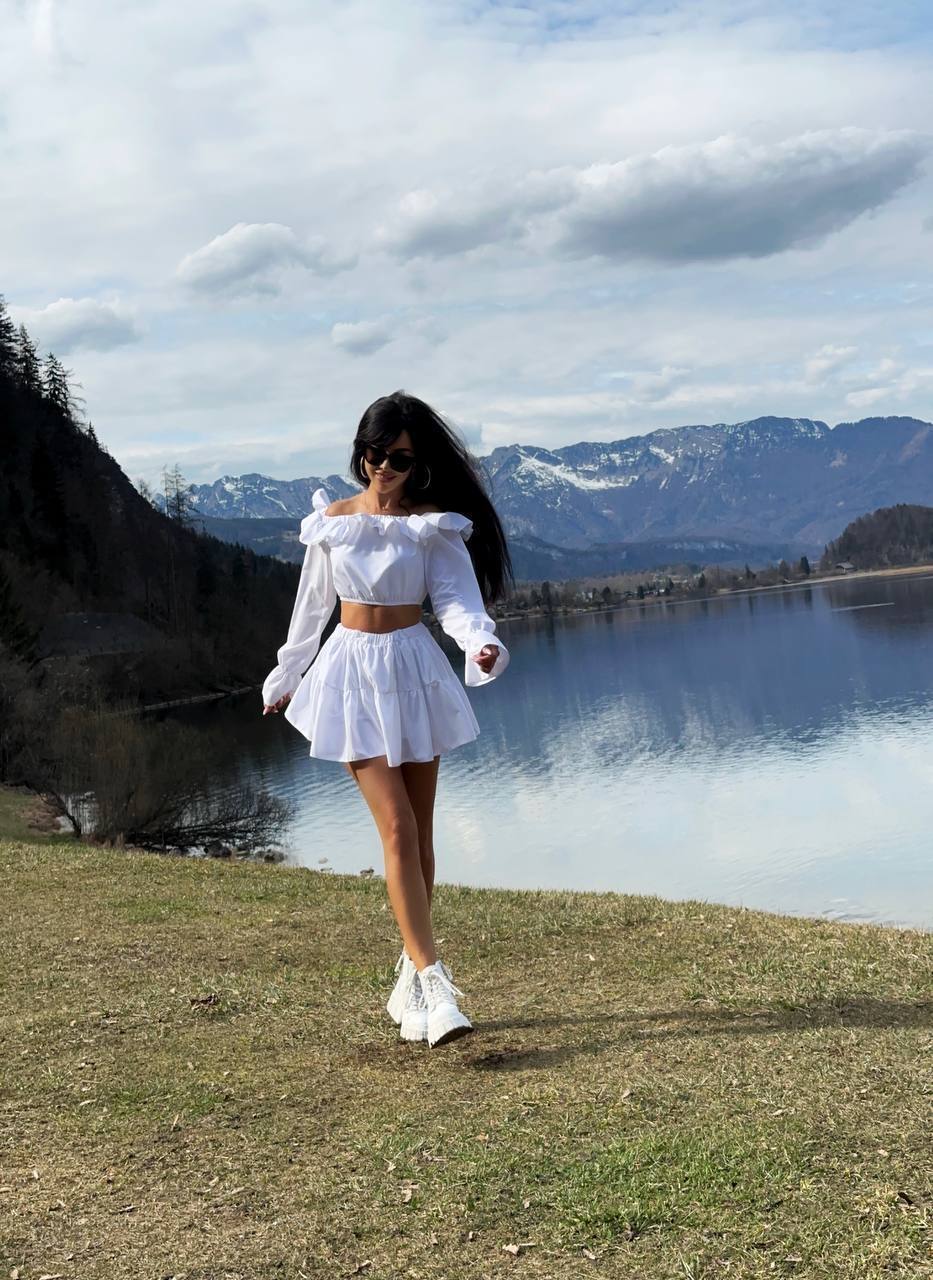 Woman in a white outfit standing by a lake with mountains in the background