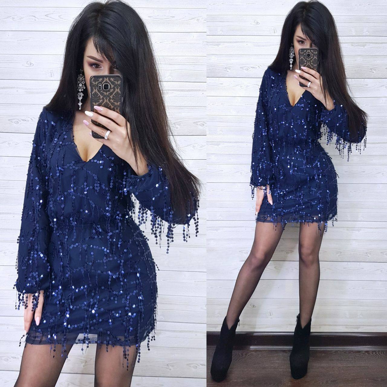 Woman wearing a blue sequin dress with long sleeves and fringe details, taking a mirror selfie.