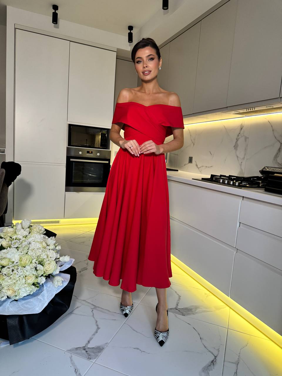 Woman in a red dress standing in a modern kitchen with white cabinets and marble floor.