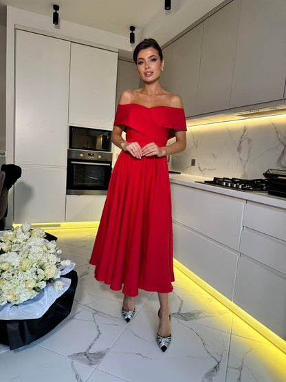 Woman in a red dress standing in a modern kitchen with white cabinets and marble floor.