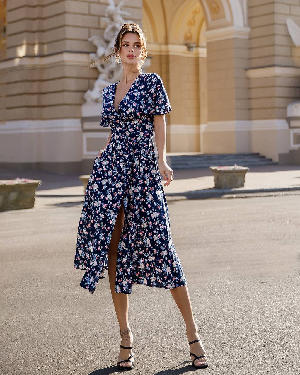 Woman in a blue floral dress standing in front of an architectural building.