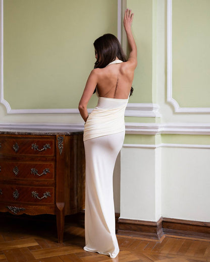 Woman in a white evening gown standing in a room with green walls and wooden furniture.