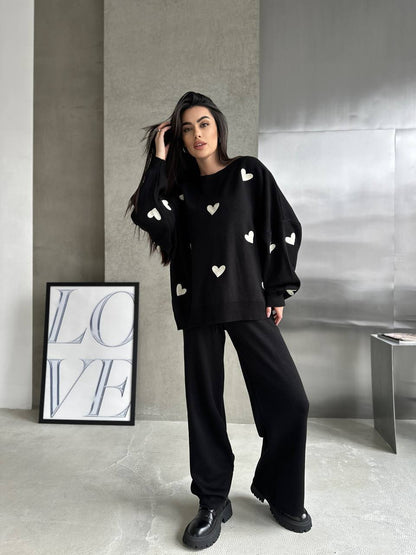 Woman wearing a black outfit with heart patterns in a minimalistic room.