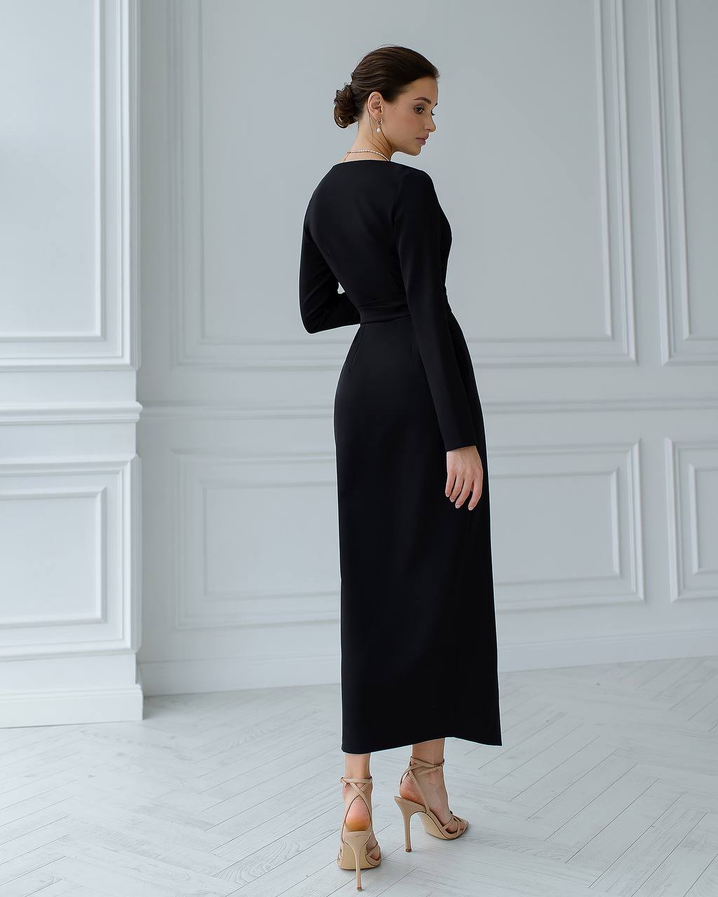 Woman wearing a black dress in a minimalistic room with white walls and floor.