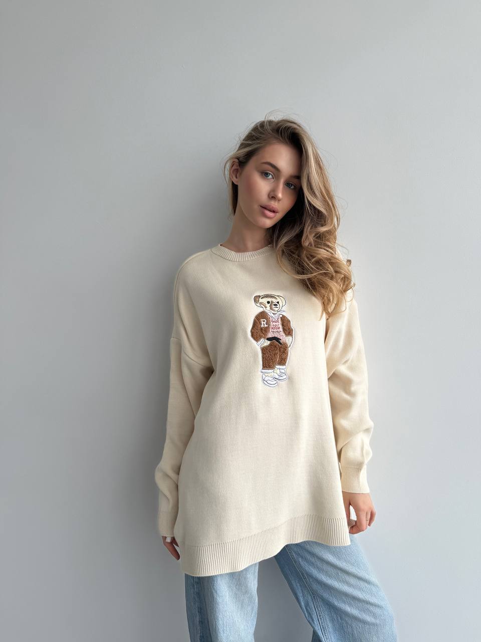 Woman wearing a beige sweater with a graphic design against a plain background